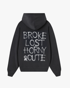 Back view of Baron & Buck Ash hoodie with bold graffiti-style text reading “Broke Lost Horny & Cute” — expressive streetwear mixing humor, chaos, and charm.