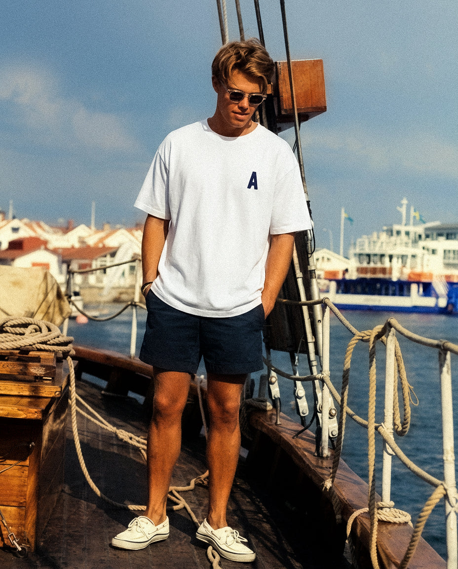 Man standing on a boat deck with a harbor in the background wearing Baron & Buck  white t-shirt with embroidered letter "A"