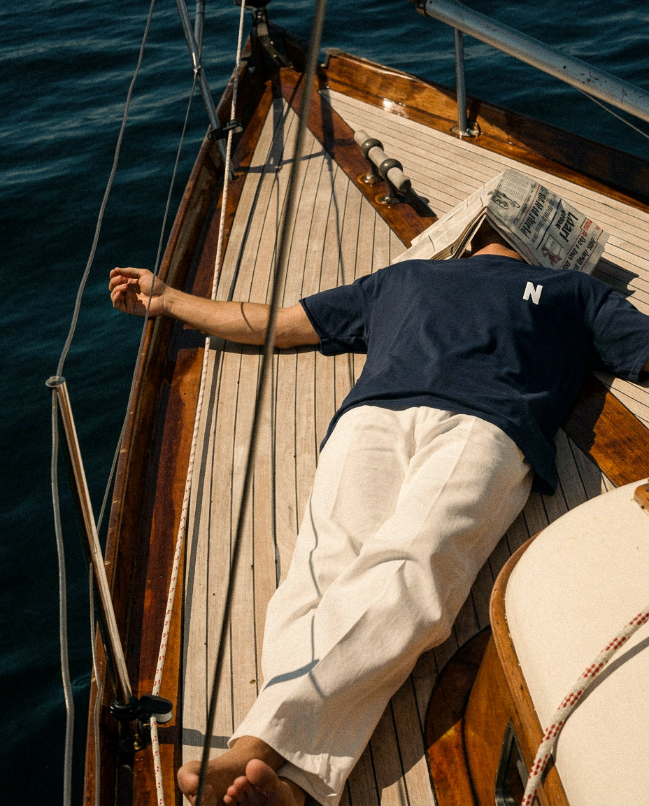 Person relaxing on a sailboat with arms outstretched, wearing  Baron & Buck  navy shirt with embroidered letter "N" and white pants.