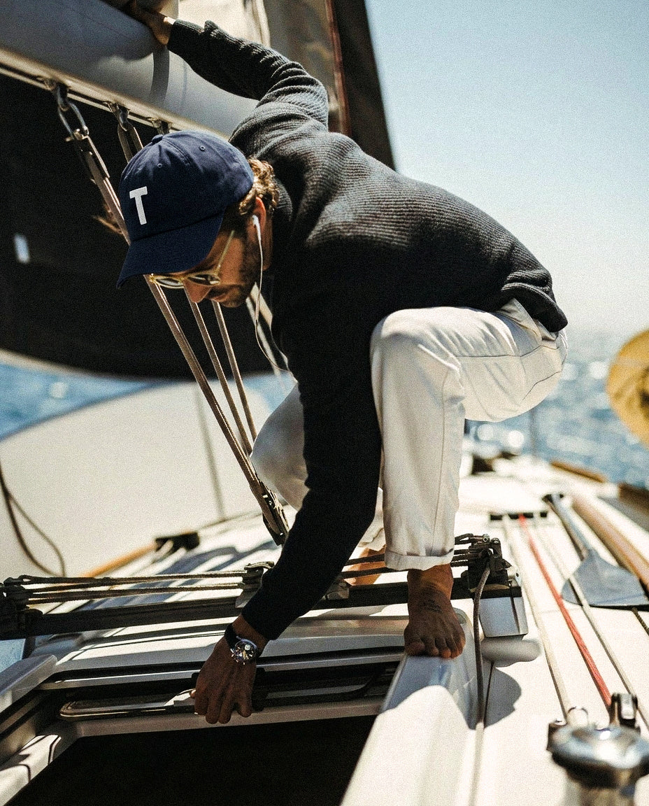 Person on a boat wearing Baron & Buck navy cap with letter "T" embroidered and sunglasses, with water and sky in the background