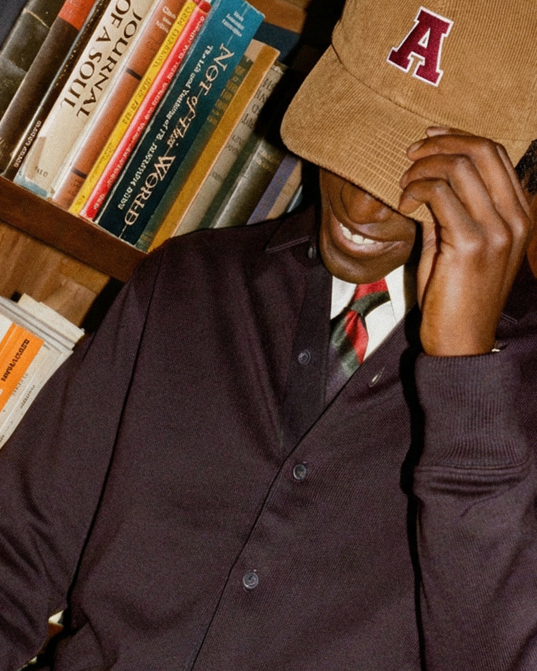 Person wearing Baron & Buck Corduroy cap cap with a letter 'A' in front of a bookshelf.